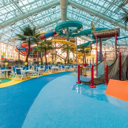 Spacious indoor water park featuring dining, colorful slides, transparent roof.