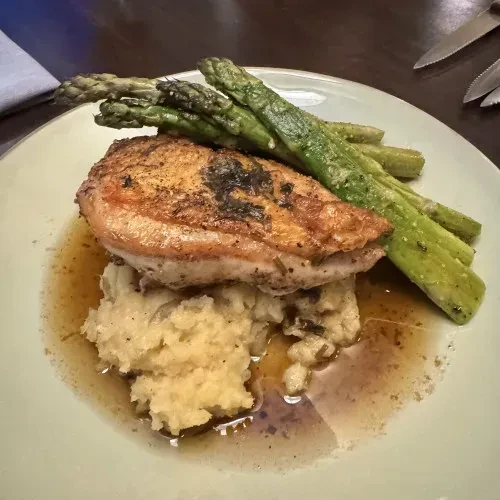 Golden-brown chicken, mashed potatoes, asparagus, and brown sauce on a plate.