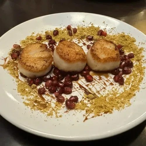 Three perfectly seared scallops with pomegranate seeds on a white plate.