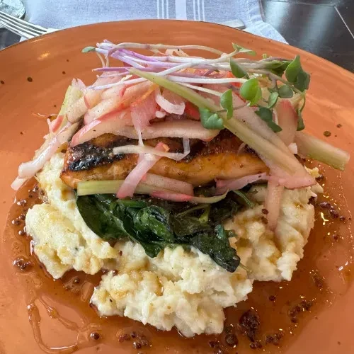 Plated seared fish with mashed potatoes, spinach, garnish, and sauce.