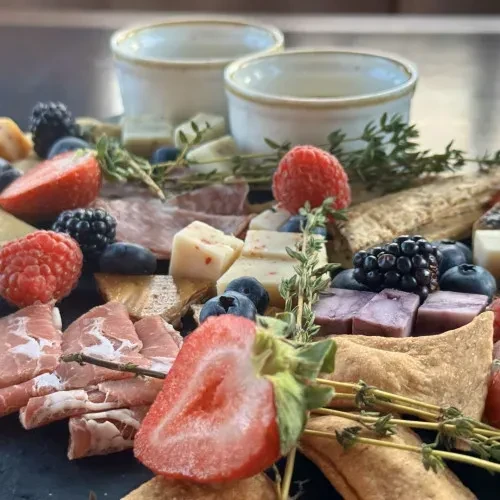Charcuterie board with sliced meats, assorted cheeses, fresh berries, and herbs.
