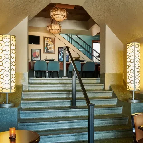 Interior features stone staircase, teal chairs, and GOLDEN SABLE poster.