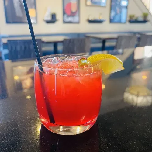 Vibrant red or pink cocktail with ice, lime, and black straw.