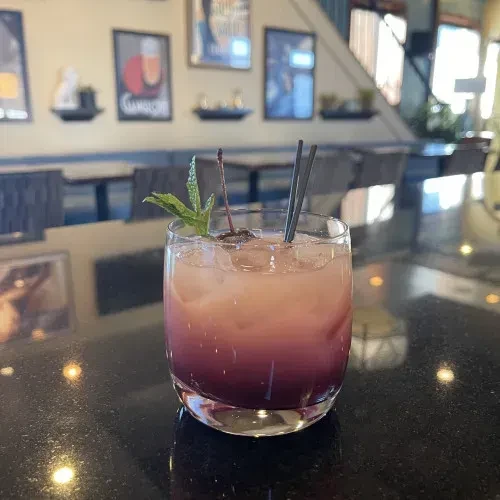 Peachy-pink to purple gradient cocktail with cherry, mint, and straws.