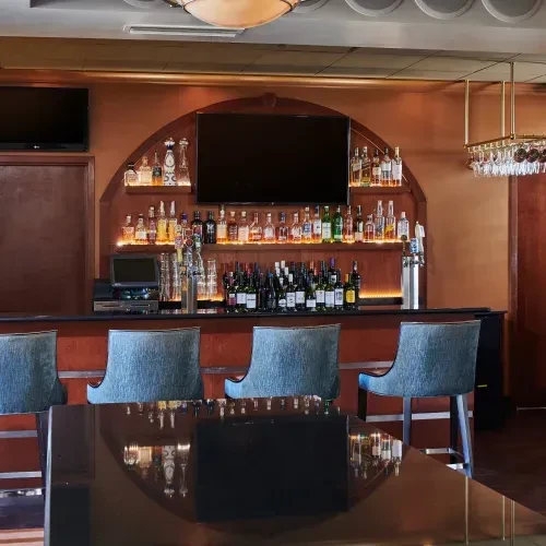 Bar with warm-toned, arched shelves displaying spirits and bar stools.