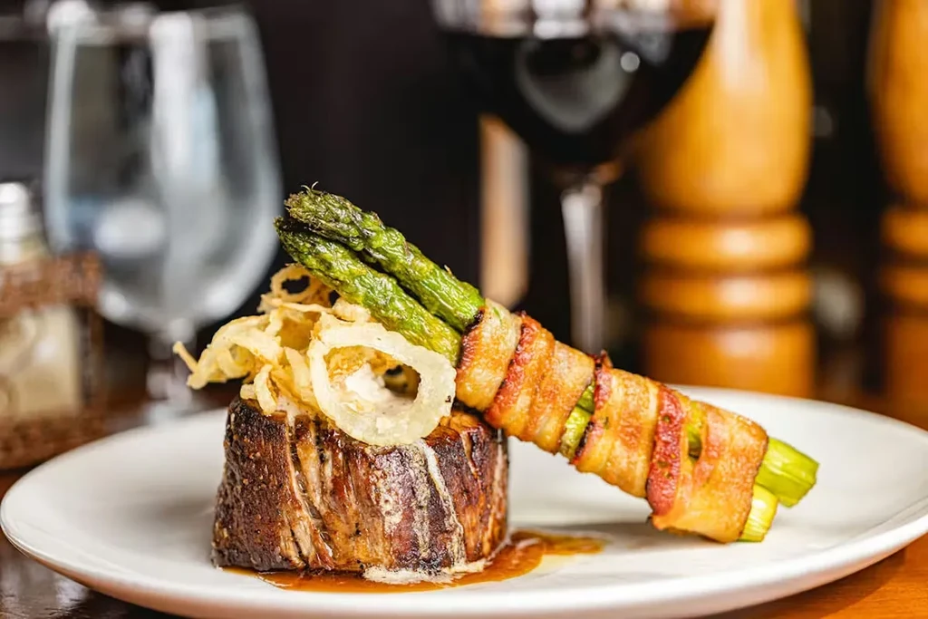 Meticulously plated steak, crispy onions, bacon-wrapped asparagus, and wine.
