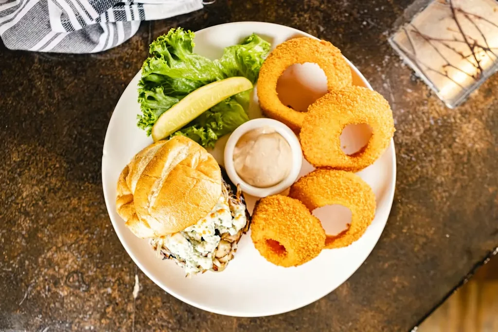 Creamy sandwich with onion rings, lettuce, pickle, and dipping sauce.