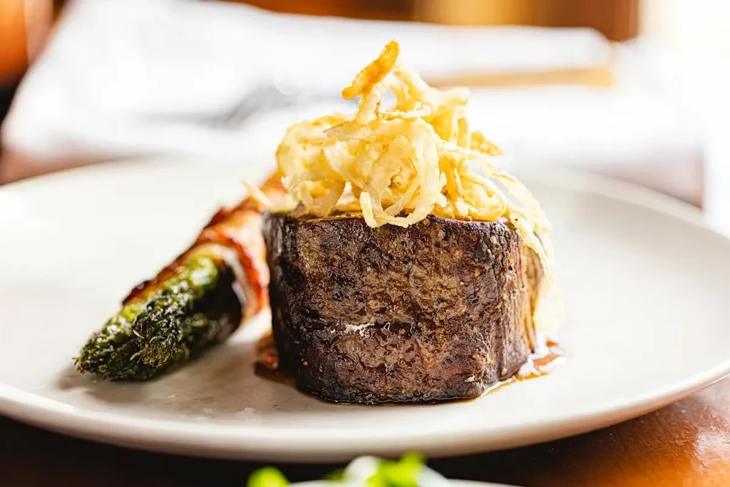 Plated seared steak with crispy onions and bacon-wrapped asparagus.