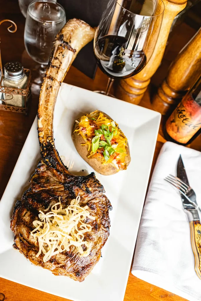 Grilled Tomahawk steak with fried onions and a loaded baked potato.