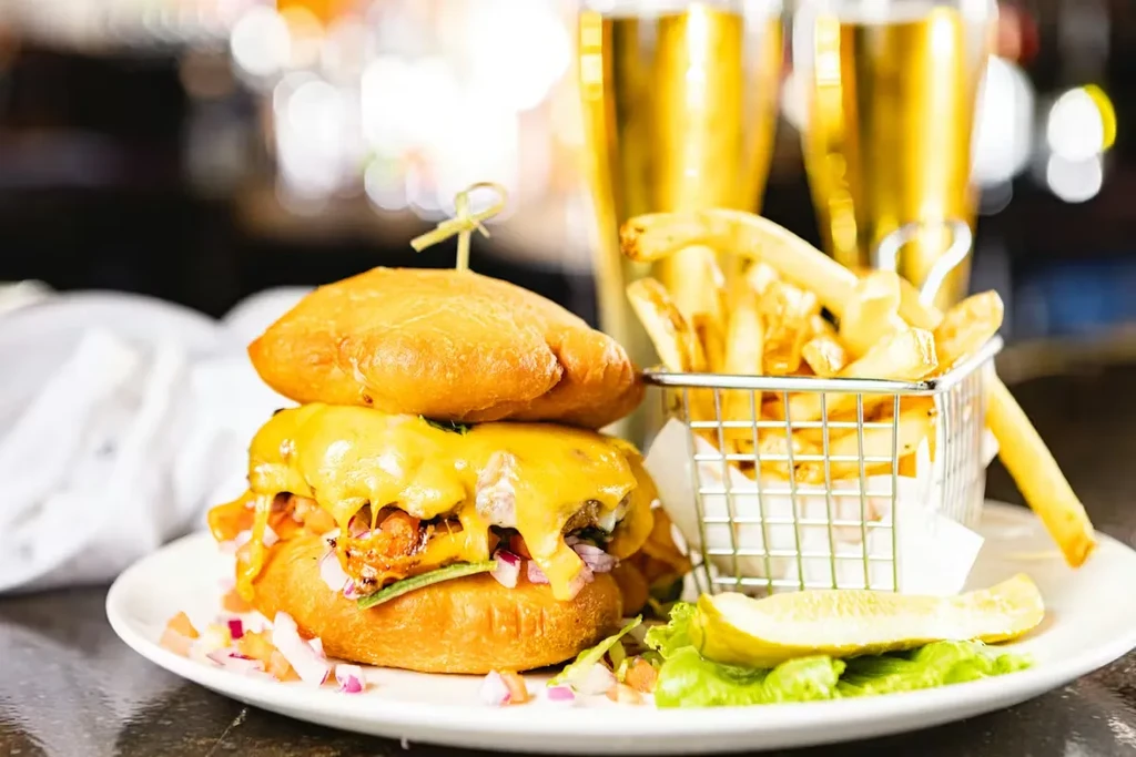 Close-up of a burger, fries, and pickle on a plate with beer.