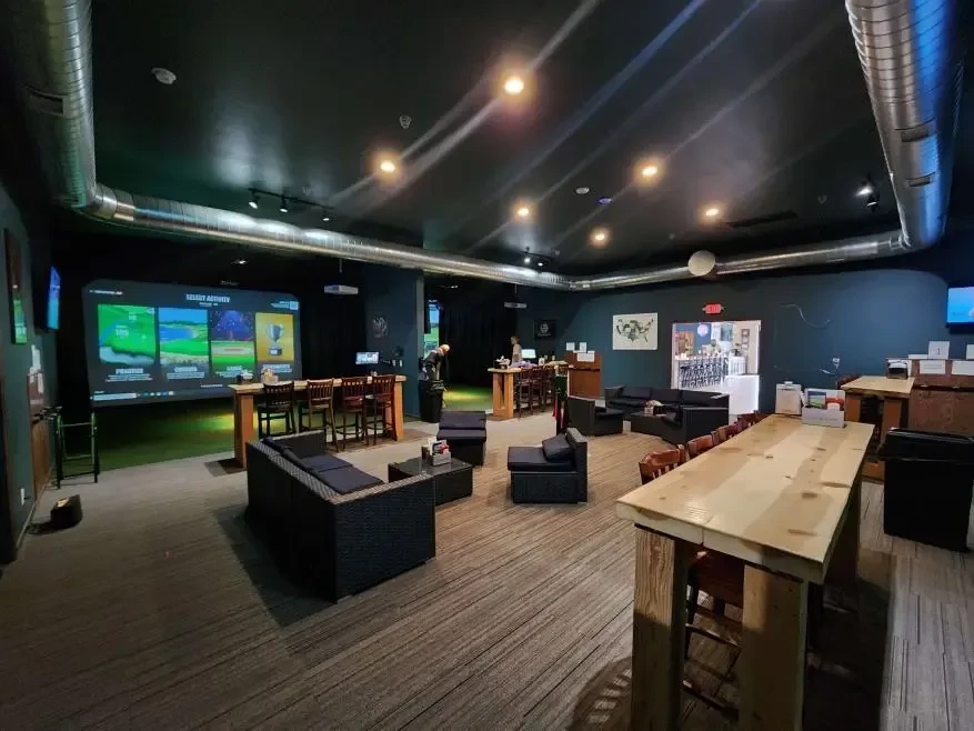 Indoor golf simulator lounge featuring dark, modern industrial design.