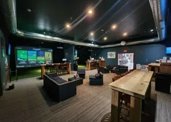 A dark, modern bar and lounge with multiple golf simulators.