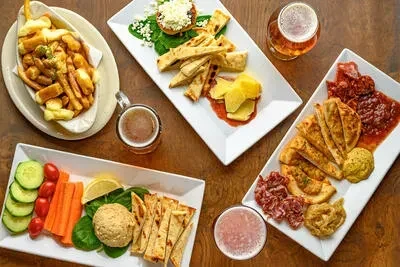 Overhead shot of appetizers, flatbread, cured meats, and drinks on table.