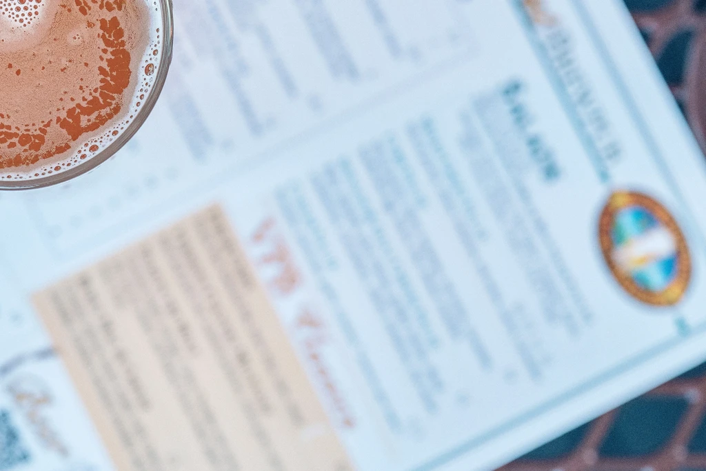 Glass of amber beer with a thick foam head, blurry menu.