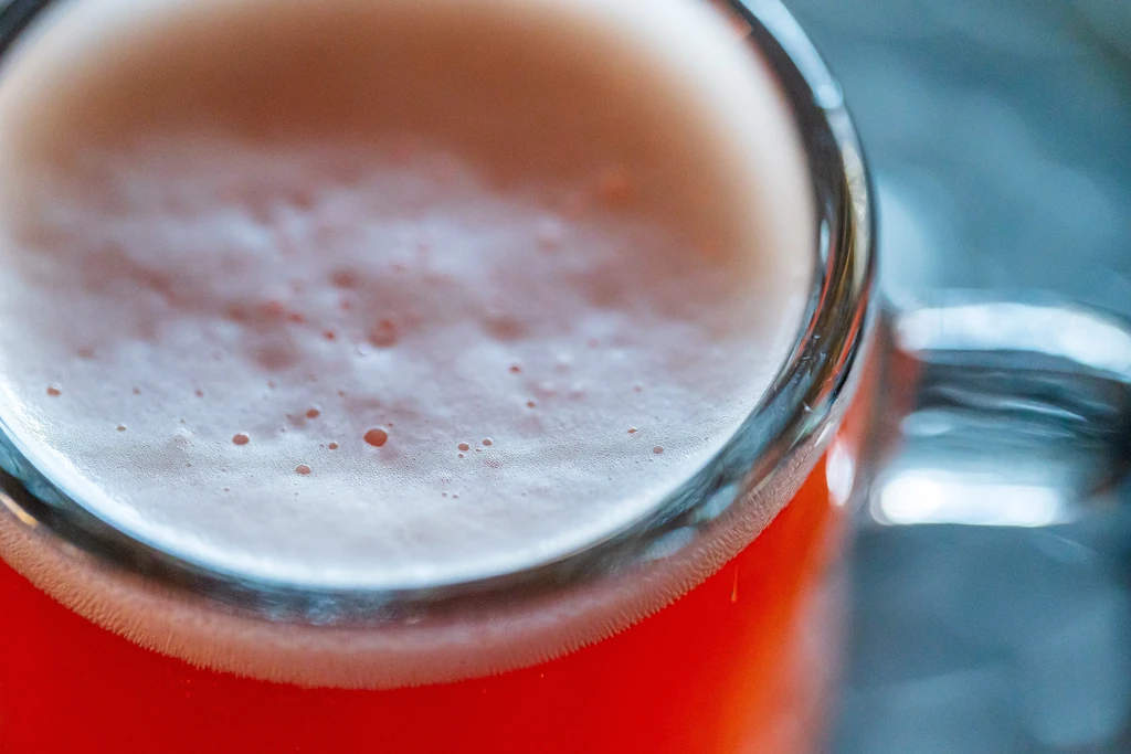 Red drink in a clear glass with frothy, light beige foam.