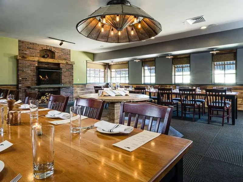 Rustic restaurant interior with communal table, fireplace, and ornate chandelier.