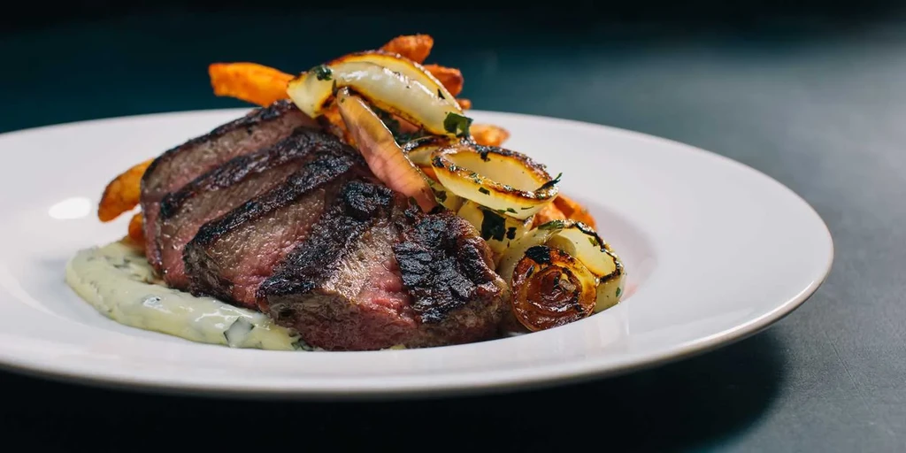 Seared medium-rare steak, sliced, with green sauce and caramelized onions.