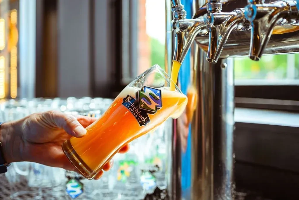 Hand pouring golden beer into a Switchback branded glass from a tap.