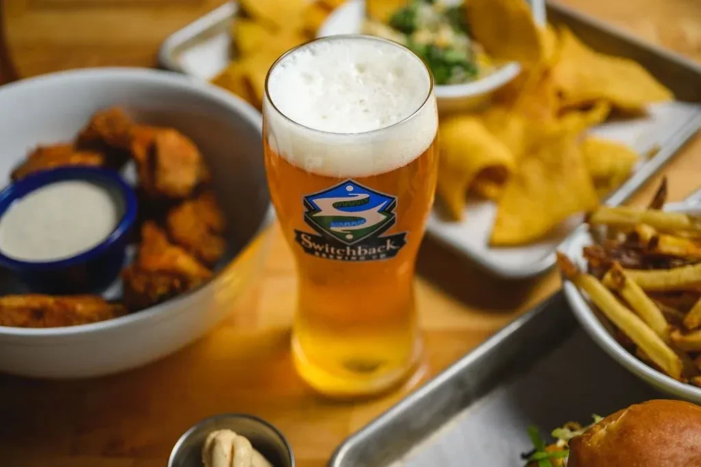 Switchback beer, chicken wings, fries, and sauces on a wooden table.