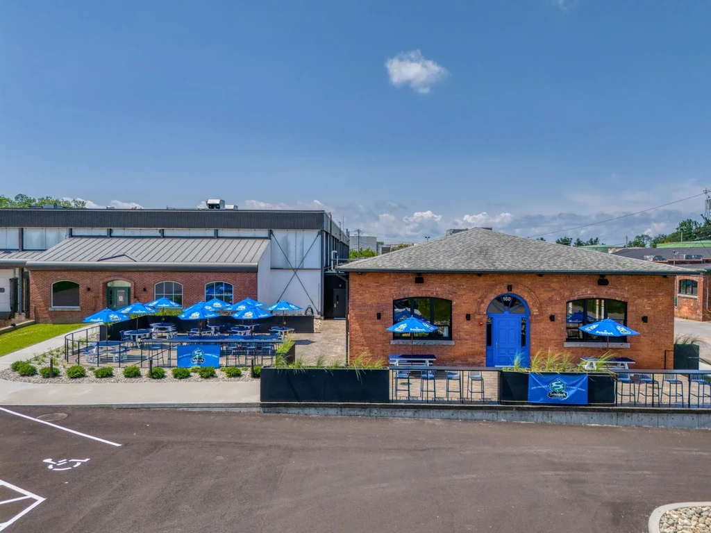 Brick restaurant complex with patios, blue umbrellas, and parking lot.