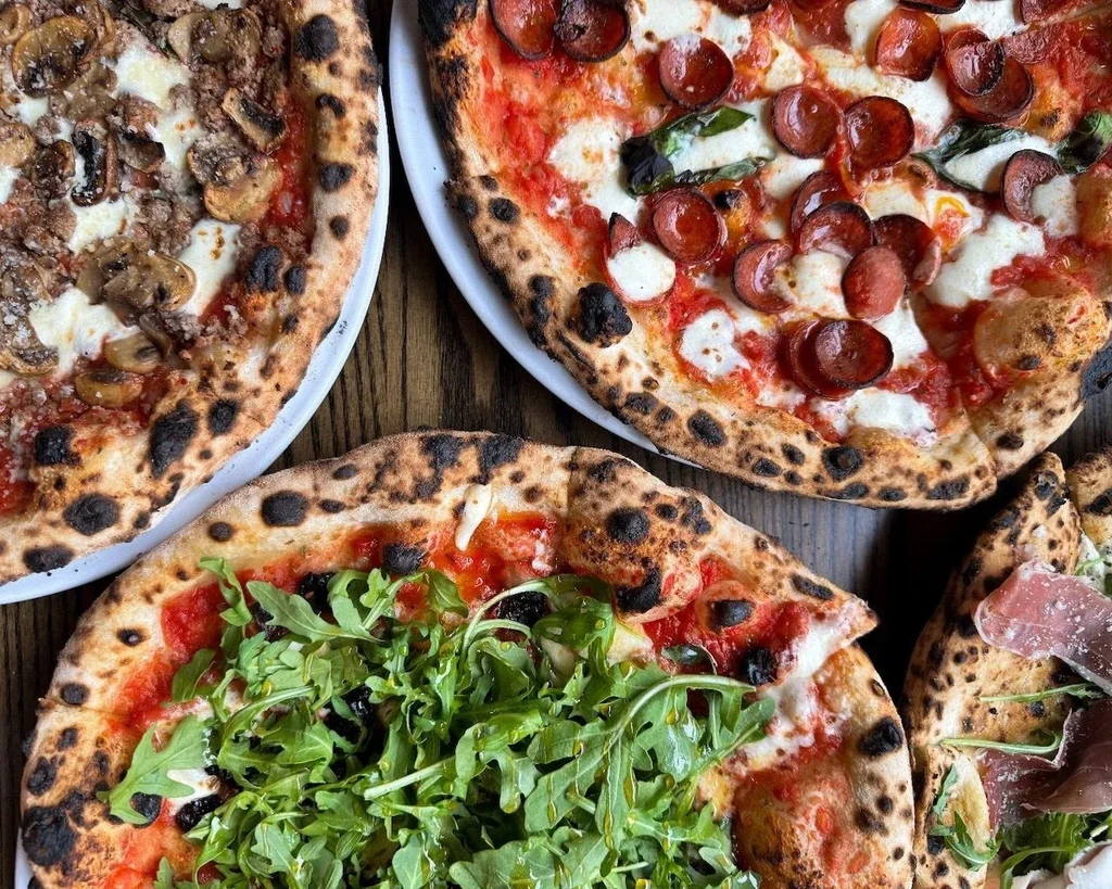 Overhead view of four distinct artisan pizzas on a rustic table.