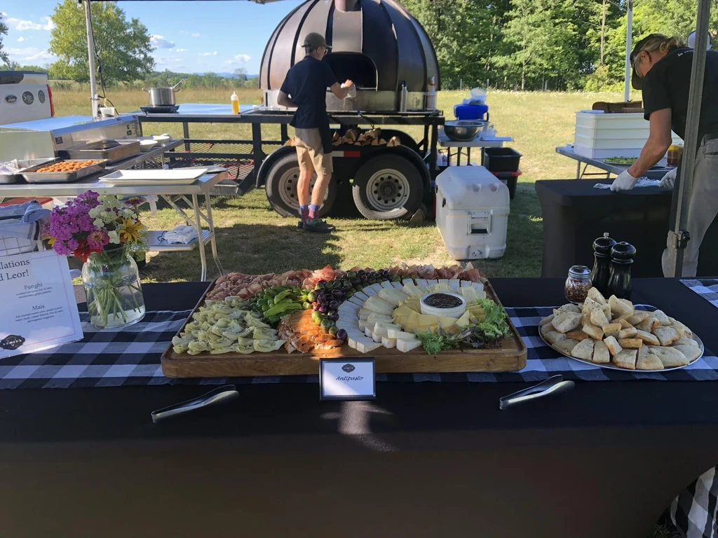 Outdoor event with a charcuterie board, focaccia, and mobile pizza oven.