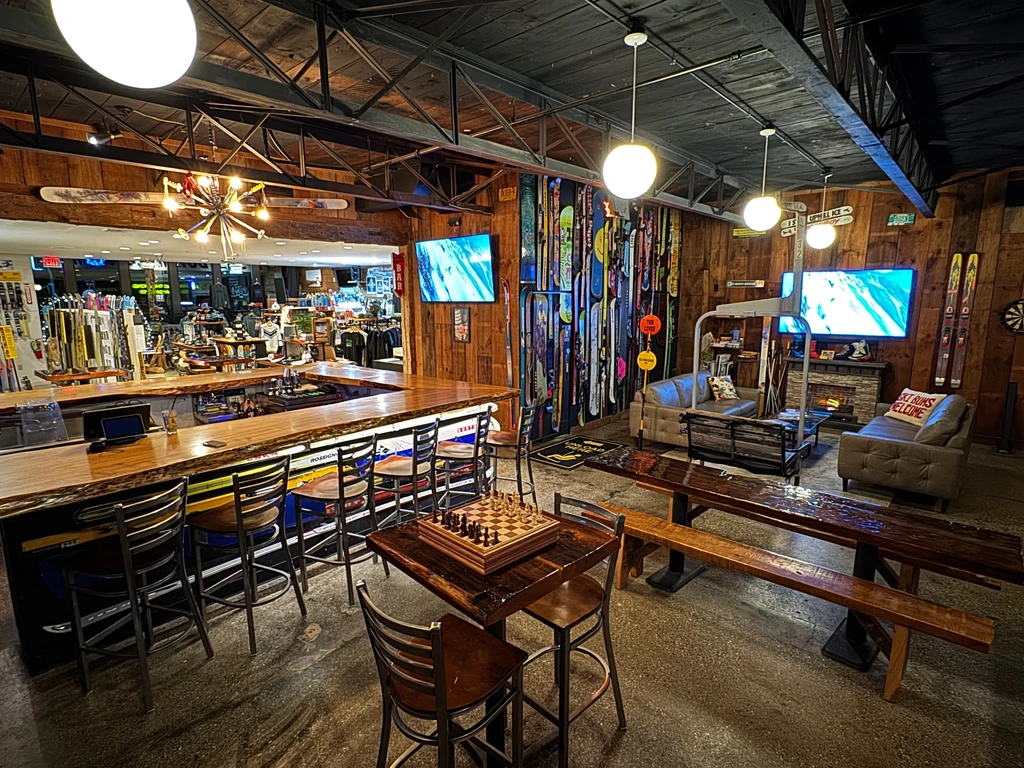 Ski lodge bar interior with a wooden bar, lounge, and ski equipment.