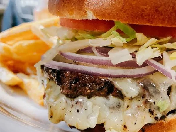 Close-up cheeseburger with melted cheese, lettuce, tomato, onion, and fries.