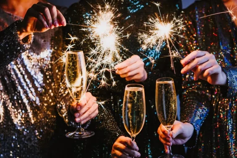 Hands holding champagne flutes and actively burning sparklers.