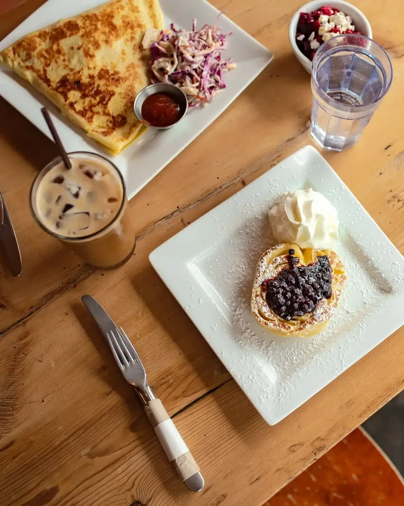 Overhead view: rustic table with crepe, berry pastry, coffee, fruit salad.