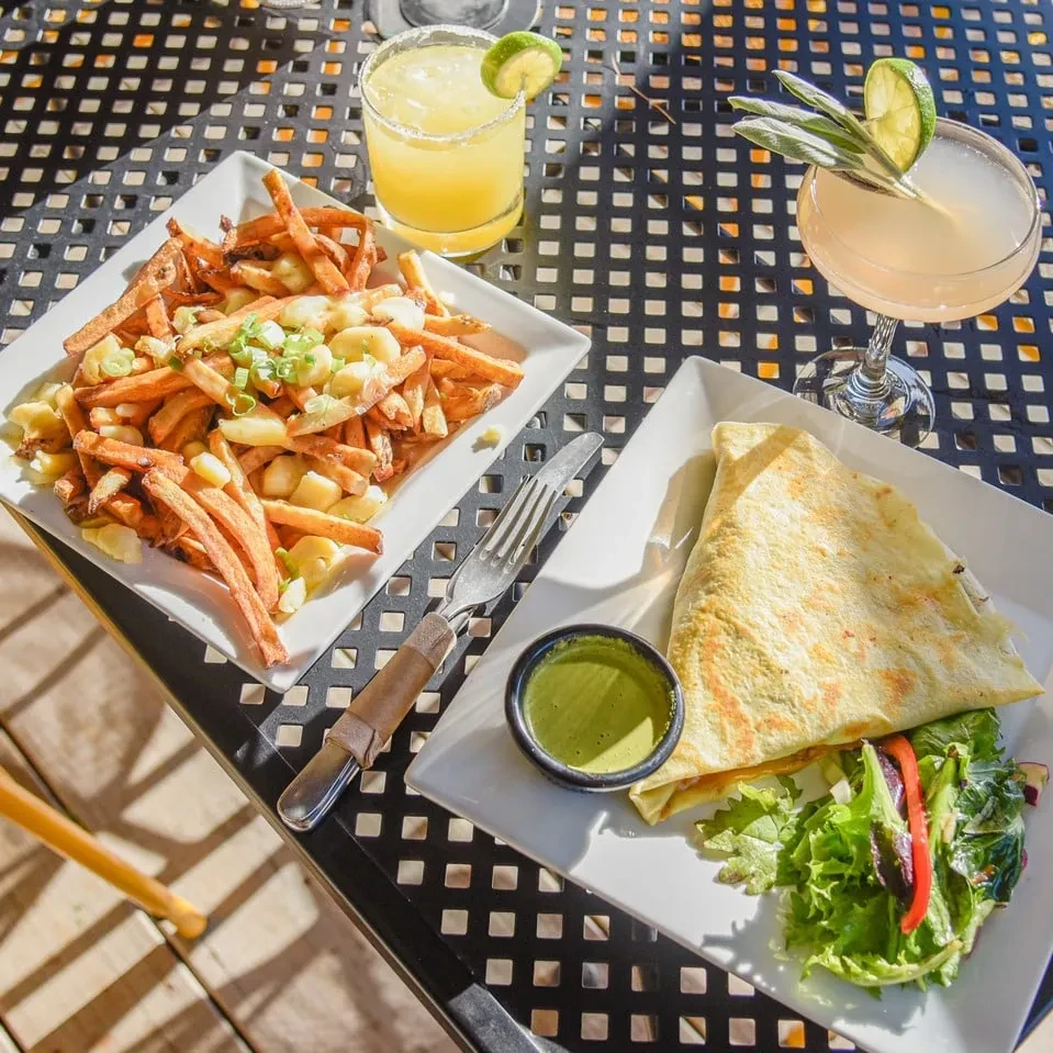 Poutine, a crepe, and two cocktails on an outdoor patio table.
