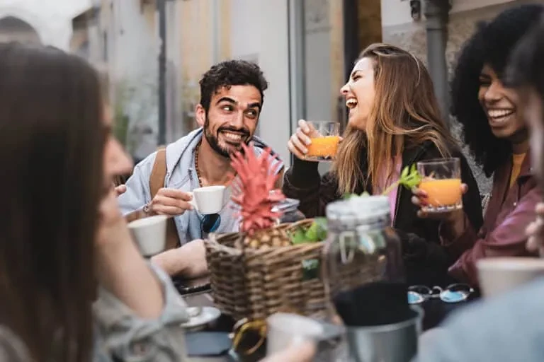 Five friends enjoying drinks and laughter at an outdoor cafe.