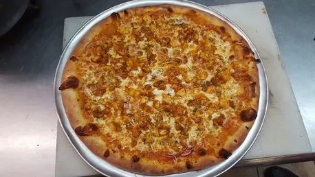 Pizza with seasoned chicken, mozzarella, onion, and herbs on a silver pan.