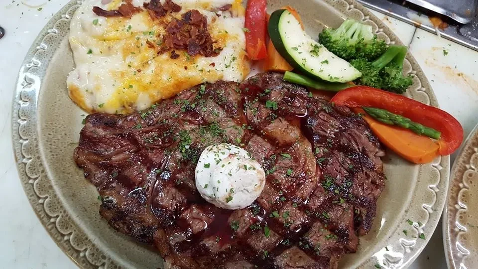 Grilled steak with herb butter, cheesy potatoes, and mixed vegetables.