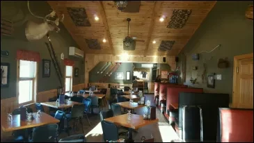 Rustic lodge dining room with wood paneling and a deer head.