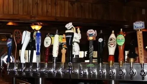 Varied, branded beer tap handles brightly lit in a dark bar.