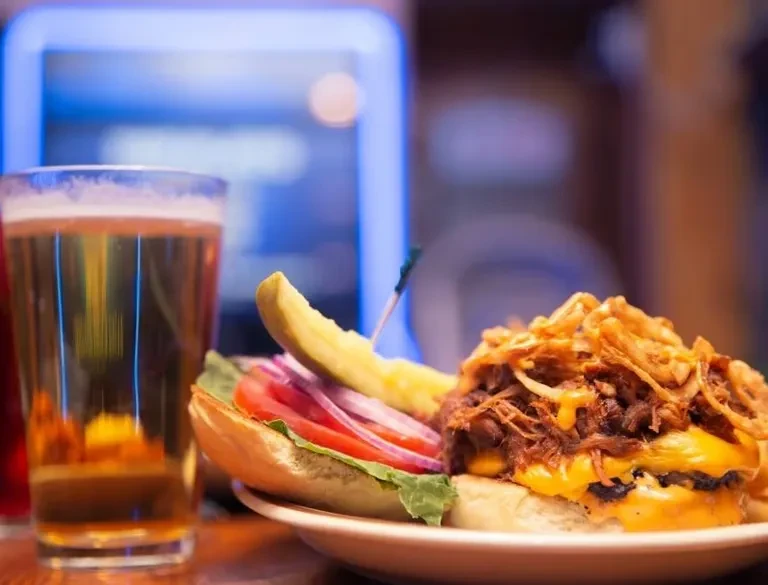 Open-faced burger with pulled meat, crispy onions, pickle, and beer.