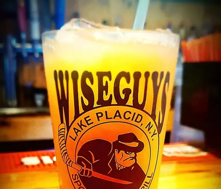 Close-up of vibrant drink with ice in a WISEGUYS logo glass.