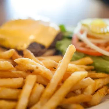 Golden-brown french fries in focus, blurry cheeseburger in background.