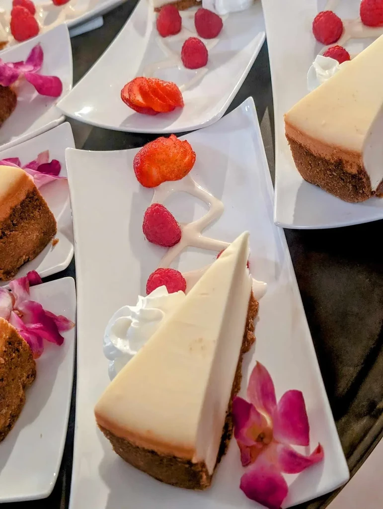 Cheesecake slices garnished with fruit, whipped cream, and orchids on plates.