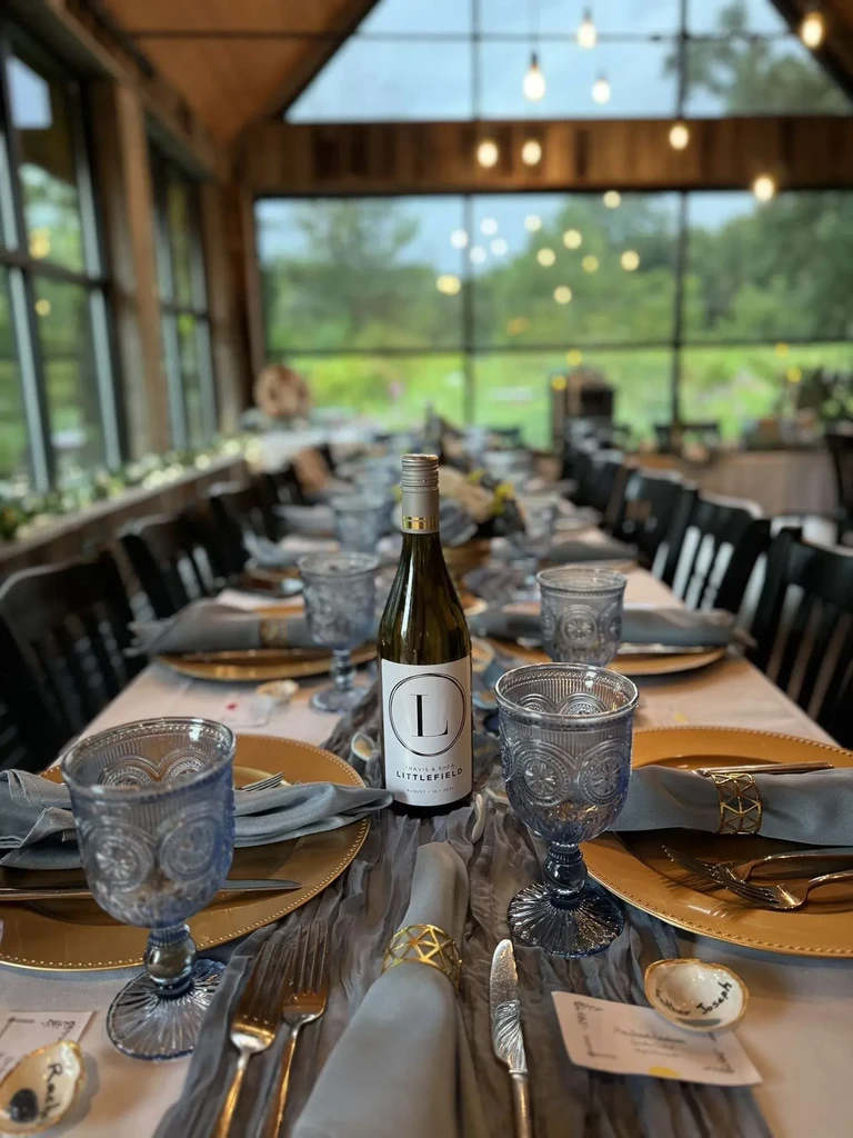 Elegant dining table with gold settings, blue glasses, and personalized wine.