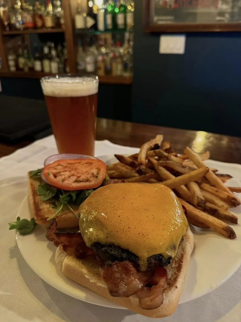 Open-faced cheeseburger with bacon, fries, and beer in a bar.
