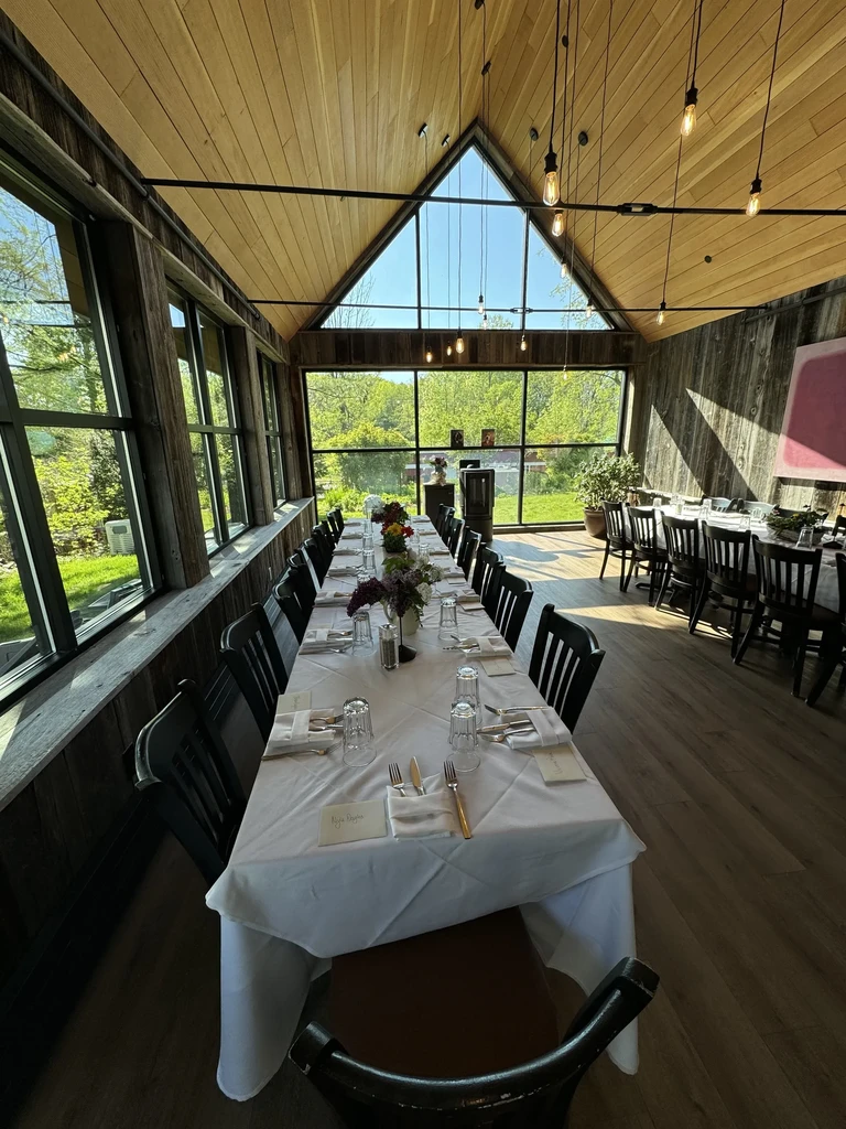 Long dining table in bright room with vaulted ceiling and green view.