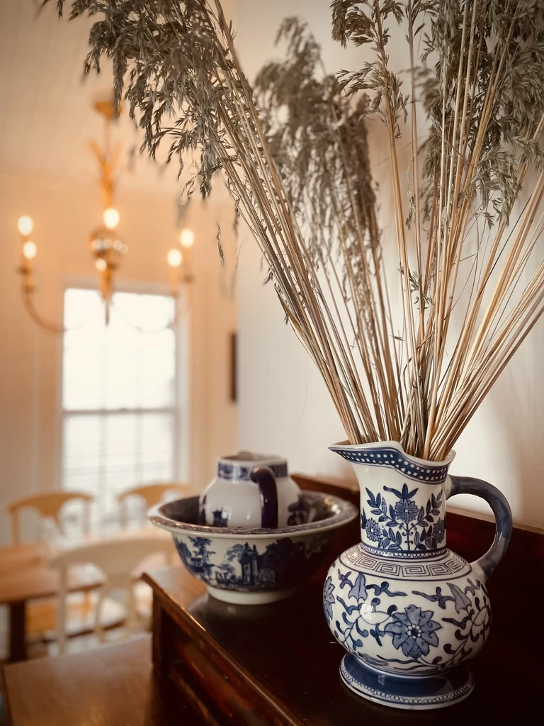 Blue and white porcelain pitcher and bowl on wood in a dining room.