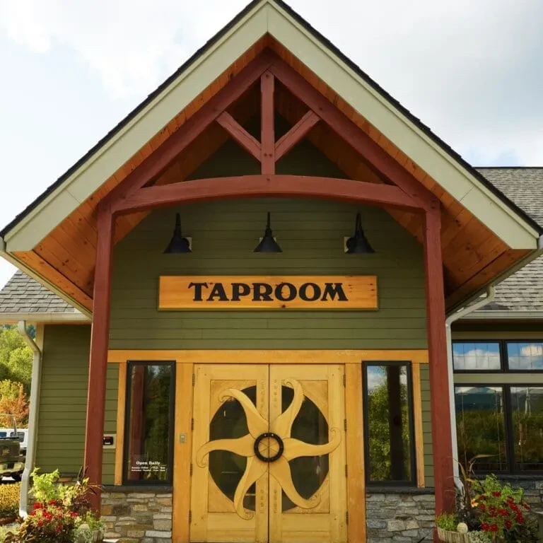 Rustic taproom building with green siding and carved sun-design doors.