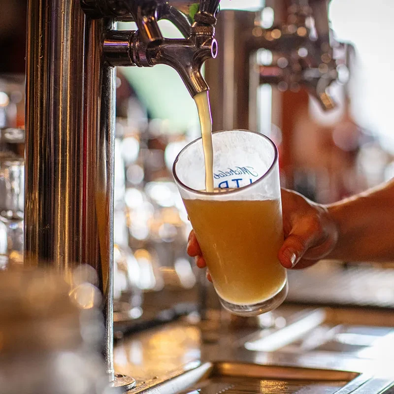 Hand holds branded glass receiving golden beverage from chrome tap.