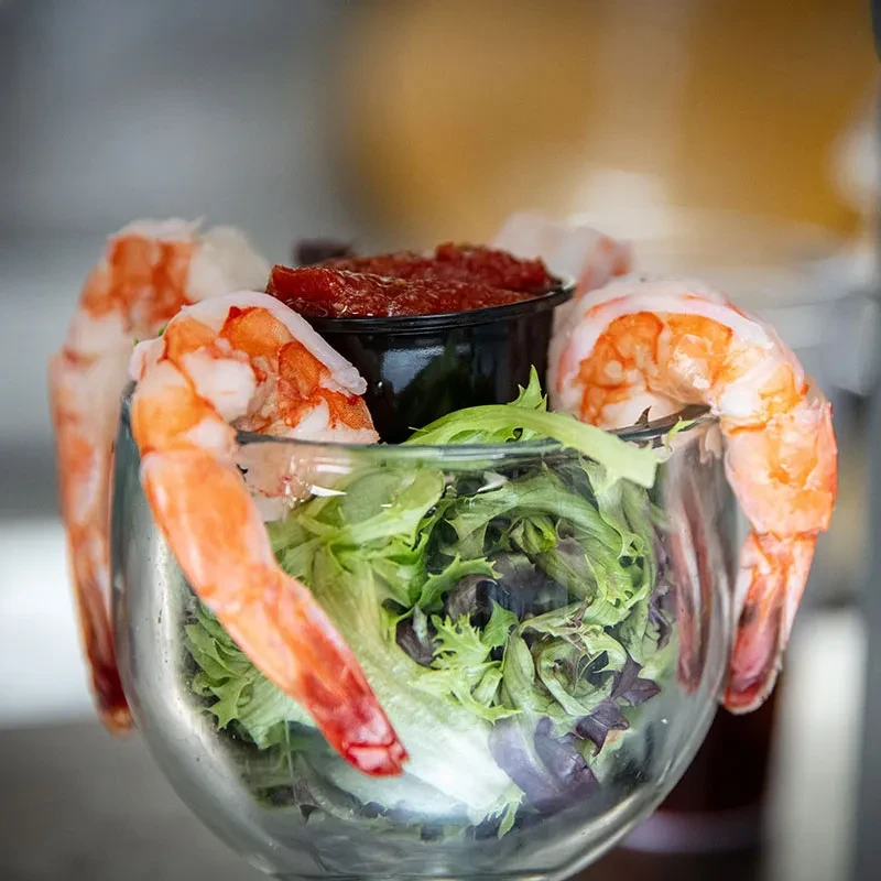 Close-up of shrimp cocktail in a footed glass with lettuce and sauce.