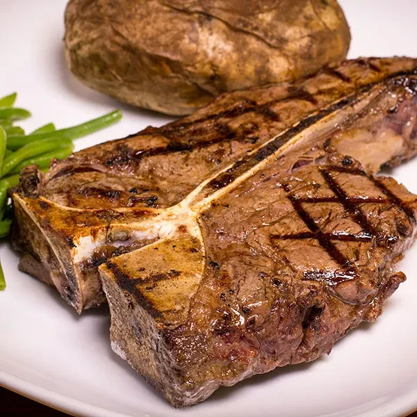 T-bone steak, green beans, and baked potato on a white plate.