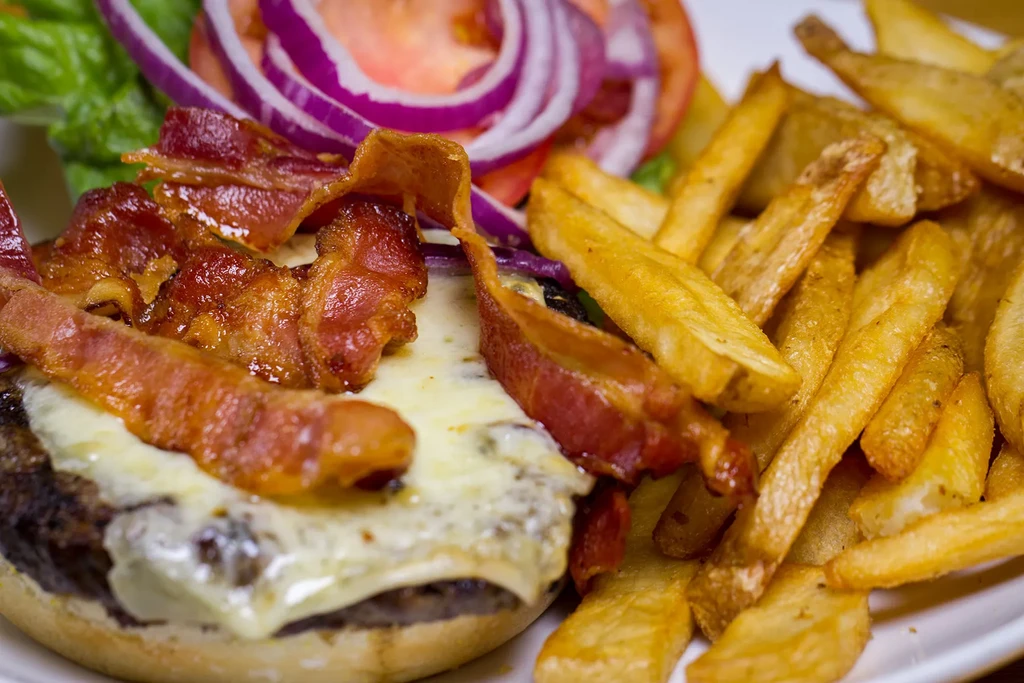 Close-up of open-faced cheeseburger with bacon, melted cheese, and fries.