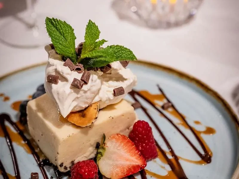 Creamy dessert slice with whipped cream, berries, chocolate, and mint.